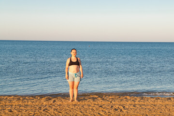 A girl in shorts and a top is standing on the seashore.