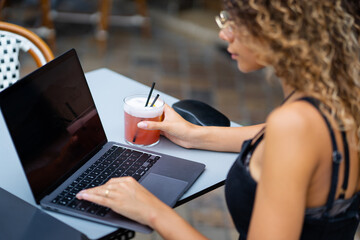 Young woman working with a laptop computer and drinking a cocktail at a bar terrace