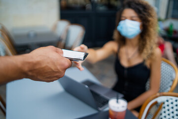 Close up on waiter's hand giving bill to a young woman wearing mask at the restaurant