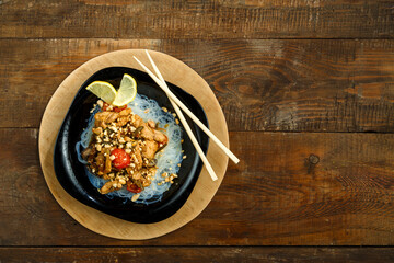 plate with funchose and chicken with vegetables in pad Thai sauce next to chopsticks on a stand.