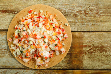 Frozen vegetables are scattered on a wooden table on a round board.