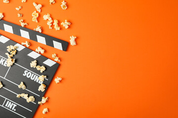 Clapperboard and popcorn on orange background. Food for watching cinema
