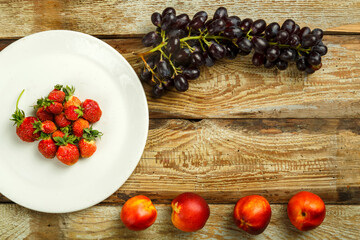Grapes and peaches and strawberries on a wooden table.