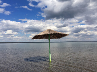  A straw umbrella stands on the shore of the salt lake of Kazakhstan against the background of a blue sky.