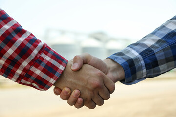 Businessmen shake hands against silos. Agriculture business © Atlas