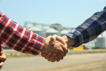 Businessmen shake hands against silos. Agriculture business © Atlas