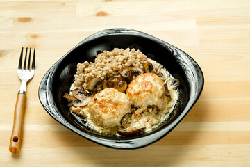 Chicken meatballs with mushrooms in a creamy sauce with a side dish of green buckwheat in a plate with a fork.