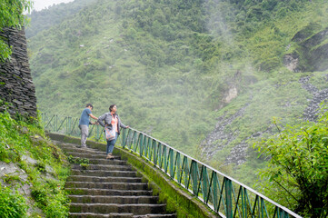 Fototapeta na wymiar Couple standing on a series of steps with clouds mist and fog on the beautiful green hills of Triund trek in McLeodganj himachal pradesh