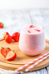 Glass with strawberry smoothie or milkshake on wooden table. Summer drink.