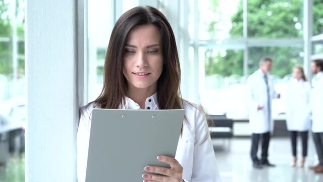 Smiling female doctor with a folder in uniform standing. Attractive doctor in white coat and stethoscope smiling at camera in clinic.