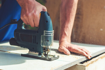 A carpenter saws a wooden cloth with an electric jig saw