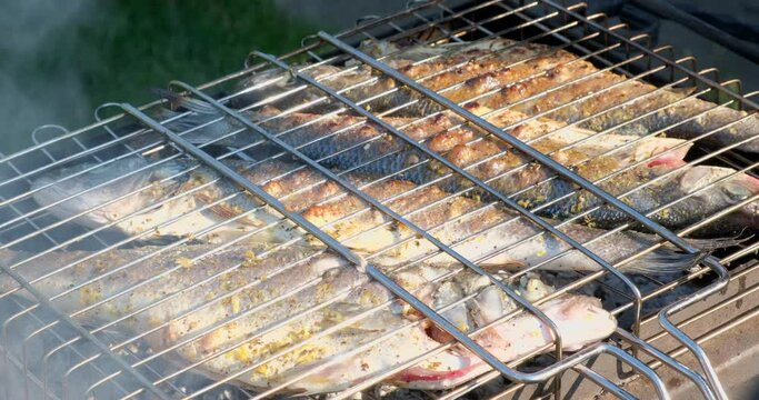 Sea bass or grouper fish grilled over charcoal. Close-up shot cooking seafish with aromatic spices on barbecue grill plate. Baking roasting marinated delicious seafood. BBQ  in summer garden outdoors 