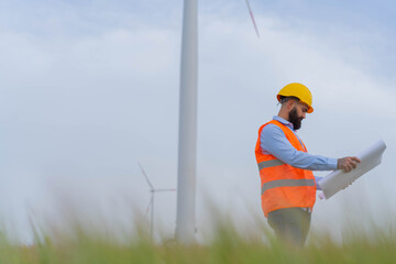 Young engineer standing in wind farm and watching plans