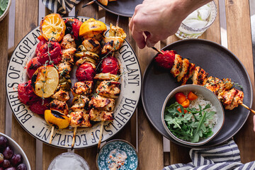Grilled chicken breast and vegetables skewers. Barbeque summer time. Party dinner. Table setting. Bright and vibrant colors. Charred veggies. Picnic scene. Lemon, artichokes, tomatoes. Weekend grill