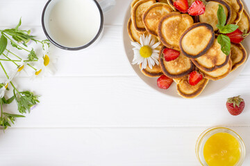 Trendy homemade breakfast with mini pancakes, honey and strawberries on a white table. View from above.