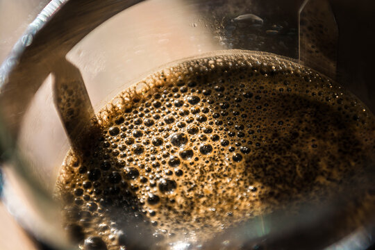 Close up of fresh coffee bubbles in a french press (sometimes called a cafetiere) in sunlight.