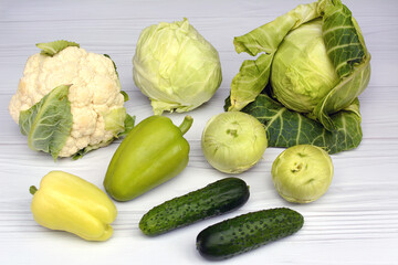 Cabbage, kohlrabi, cauliflower, cucumbers, peppers on a light wooden background. Close up