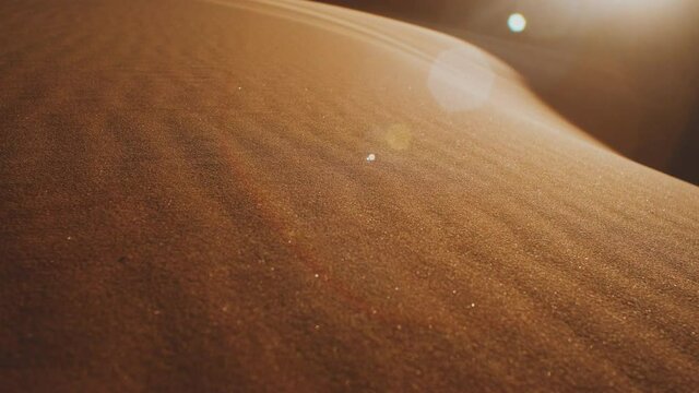 Close-up of wind blows sand in the desert of sand dunes in the Sahara desert at sunset, sun bunnies into camera, 4k