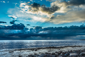 The sea after a storm over the Swedish Baltic Sea at sunset where the sun's rays light up between the clouds and the sky starts to turn blue again late at night