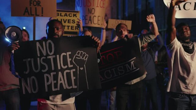 Group of multi-ethnic protests striking for human rights at night demonstration. Vigorous crowd of young people rebelling against police injustice, racism and brutality.