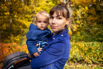 portrait of a young beautiful mother holding a toddler in her arms, dressed in a blue family look smiling and looking at the camera n autumn park