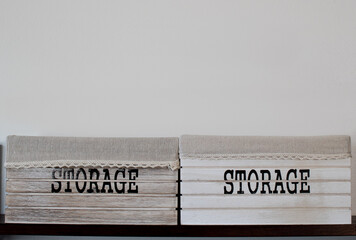 Two wooden boxes on shelf with the word storage painted in big bold black letters, cloth and lace decorative top border. White wall background with empty space for text. Organization and store concept