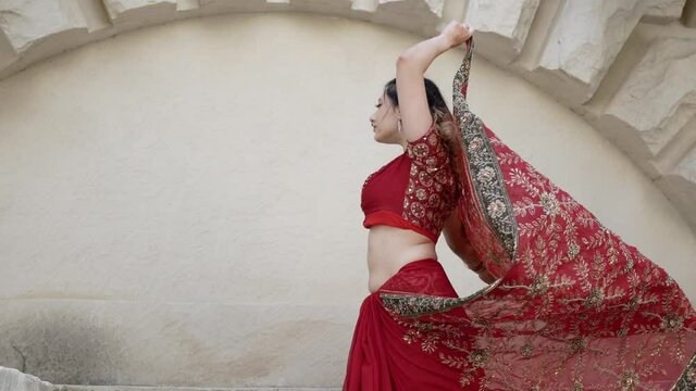 Indian woman dance on streets of ancient architecture city of India dressed in red Sari, decorated with traditional ornaments and Mehendi patterns henna drawings on hands