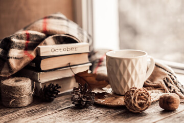 Details of still life on window. Book with scarf and cup of tea on wood background. Autumn mood.