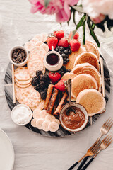 Fototapeta na wymiar Breakfast platter. Table setting. Pancakes, breakfast sausages, berries, fruits, chocolate spread and coffee. Morning light. White and grey colors. Peonies. Summer time. Sunday brunch party. Weekend