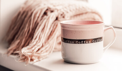 Details of still life on window. Pink mug with knitted scarf.