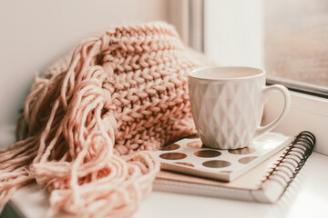 Details of still life on window. Beautiful pink mug of tea with notebook and knitted scarf. Pink mood.