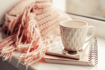 Details of still life on window. Beautiful pink mug of tea with notebook and knitted scarf. Pink mood.