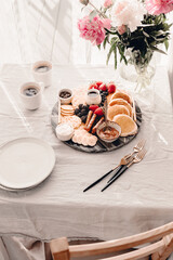 Breakfast platter. Table setting. Pancakes, breakfast sausages, berries, fruits, chocolate spread and coffee. Morning light. White and grey colors. Peonies. Summer time. Sunday brunch party. Weekend