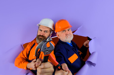 Two Repairman working with repair tools. Through paper. Advertising. Worker in helmet. Repairman. Hammer. Spanner. Wrenches. Builder in construction helmet. Hard hat. Bearded repairman.