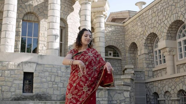 Indian woman dance on streets of ancient architecture city of India dressed in red Sari, decorated with traditional ornaments and Mehendi patterns henna drawings on hands