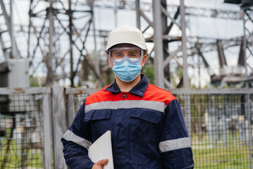 An electrical substation engineer inspects modern high-voltage equipment in a mask at the time of...