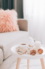 Cup of hot drink and teapot on a serving tray on table. Cozy autumn or winter concept.