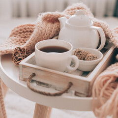 Cup of hot drink and teapot on a serving tray, knitting clothes. Cozy autumn or winter concept.
