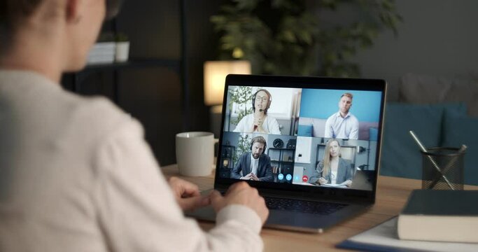 View of computer screen with four business people having working conference through video chat. Close up of woman sitting at home office with laptop and talking with coworkers.