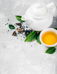 Herbal tea, cups and teapot with leaves on grey concrete background. Flat lay.