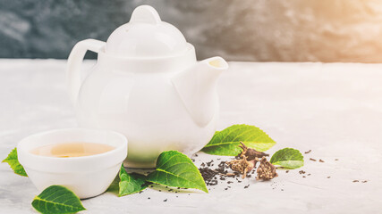 Herbal tea, cups and teapot with leaves on grey concrete background. Flat lay.