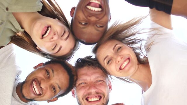 Close portrait of five young students, tolerance and no racism concept. Interracial group of students leaned over the camera against the sky