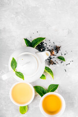 Herbal tea, cups and teapot with leaves on grey concrete background. Flat lay.