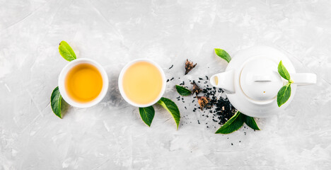Herbal tea, cups and teapot with leaves on grey concrete background. Flat lay.