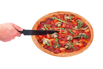 Man's hand cuts the pizza hot with the kitchen knife, angle view. Italian pizza with spicy salami, arugula, cherry tomatoes, mushrooms and texas spice mix, isolated on white background