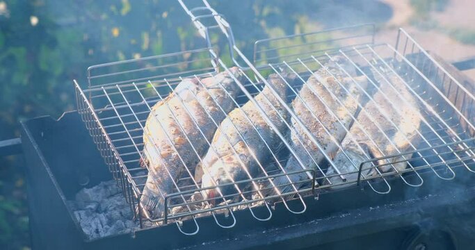 Sea bass or grouper fish grilled over charcoal. Close-up shot cooking seafish with aromatic spices on barbecue grill plate. Baking roasting marinated delicious seafood. BBQ  in summer garden outdoors 