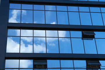 facade of a modern building on a bright Sunny day, blue sky and clouds reflecting in a glass, beautiful exterior of the new building