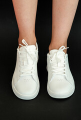 White women's sneakers dressed by a girl on a black background