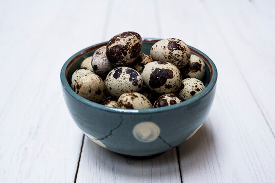 Close up of quail eggs in blue bowl on white wooden table.