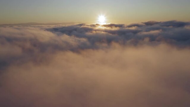 Flying through heavenly amazing sunny cloudscape toward the sun rising over the horizon and shining through the golden fluffy fog. Beautiful timelapse of clouds moving softly on the sky. 4K B roll